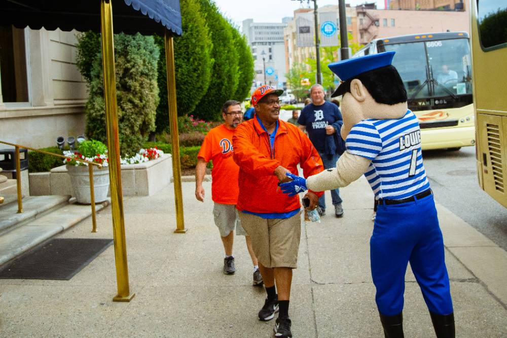 Louie the laker shaking hands with a tigers fan as they walk to the game